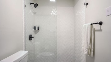 A modern shower with a glass door, a white tiled wall, and a towel rack.