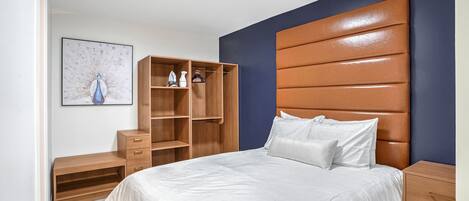 A bedroom with a large bed, wooden wardrobe, and a wall-mounted shelf.