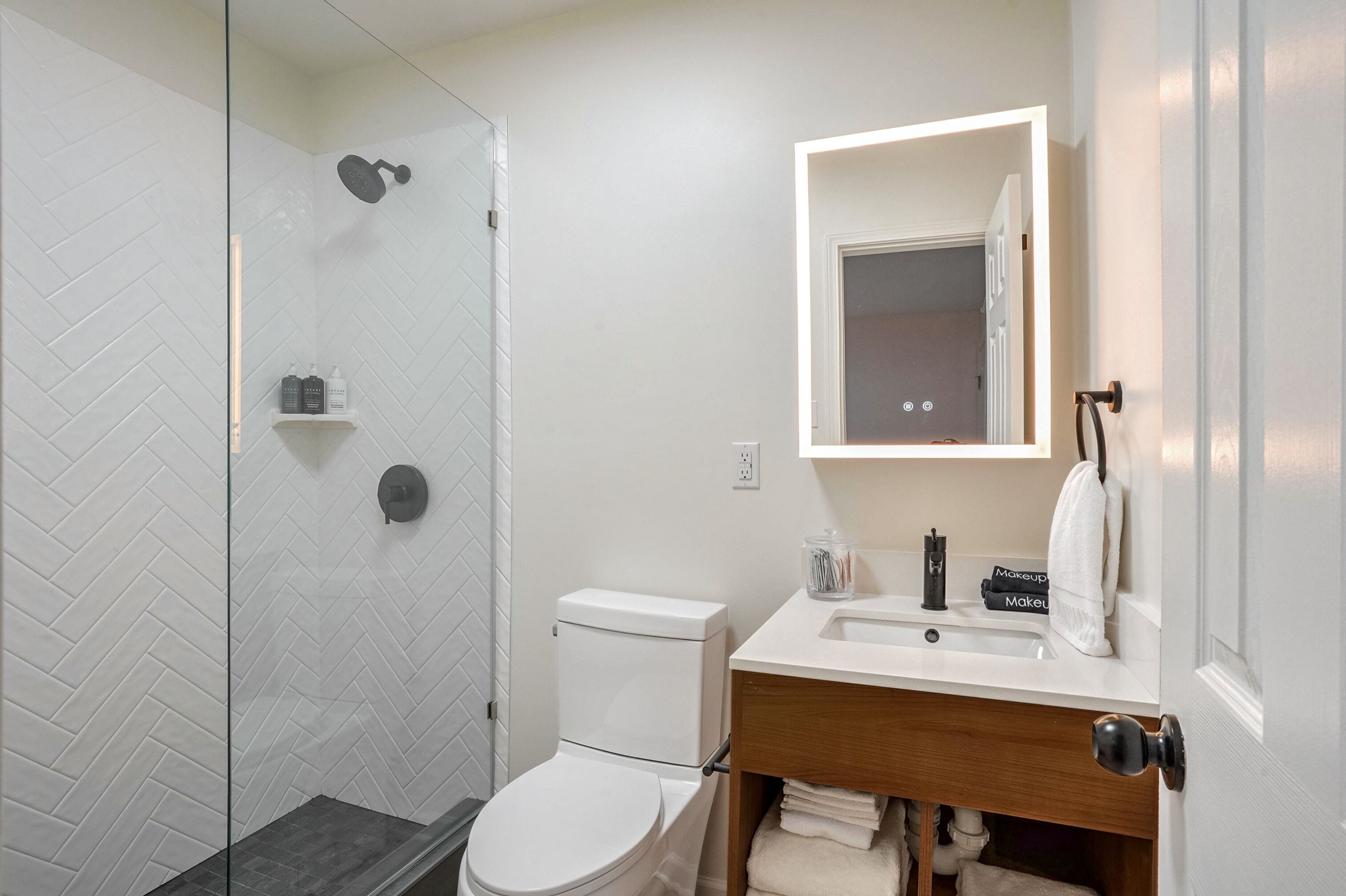 A modern bathroom with a glass shower enclosure, a white toilet, a wooden vanity with a sink, and a mirror above the vanity.