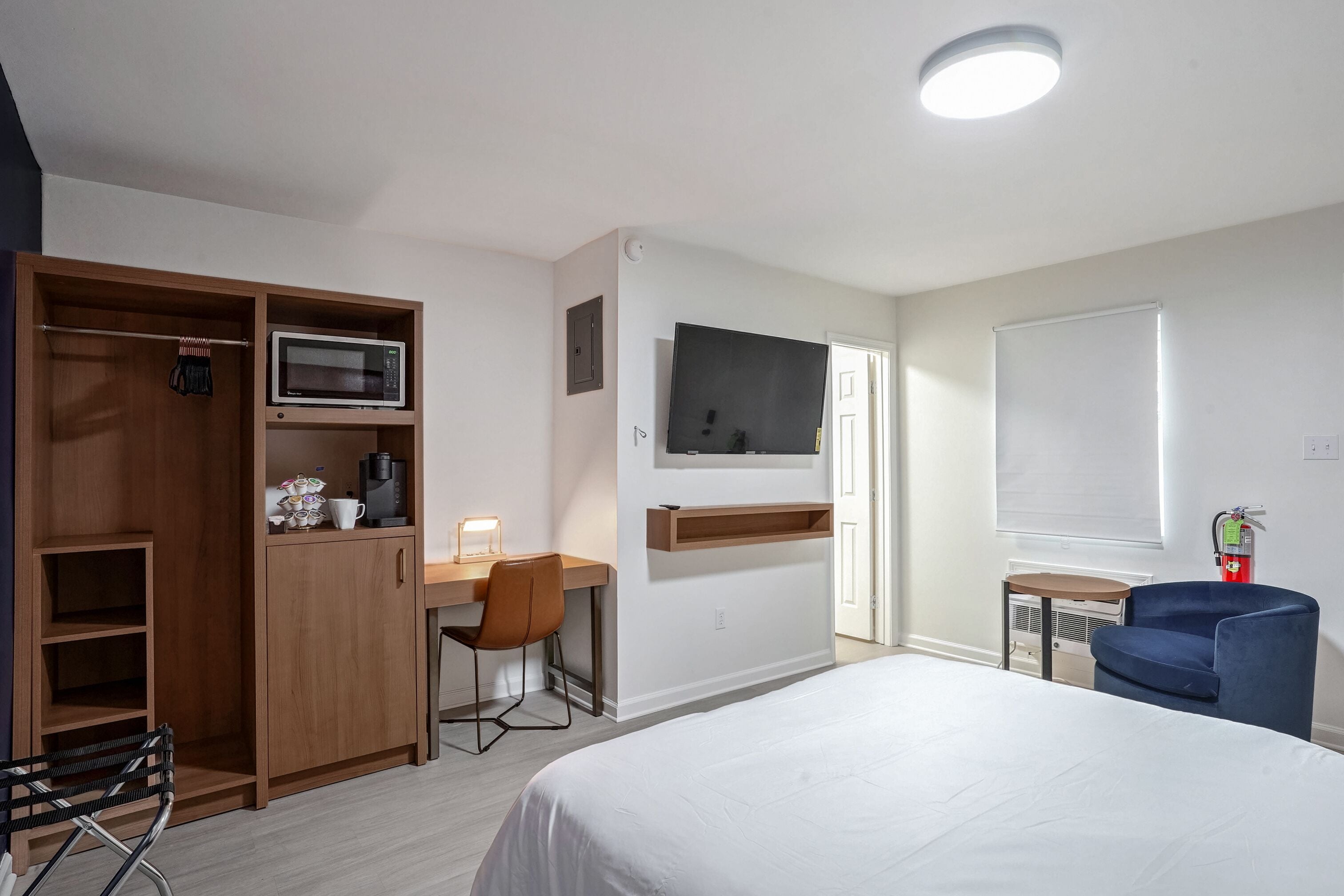 A hotel room with a bed, a desk with a chair, a wardrobe, a TV, and a small table.