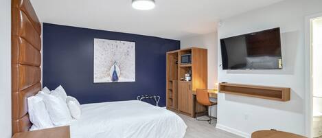 A modern hotel room with a large bed, a desk, a TV, and a wardrobe.