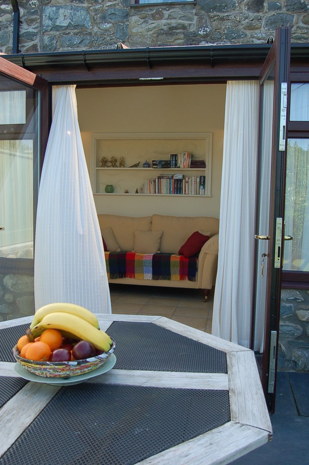 Un comedor con una mesa preparada para una comida, un frutero y vistas a una sala de estar acogedora con un sofá y estanterías.