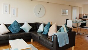 Ein modernes Wohnzimmer mit einer Ledersofa, einer runden Wanduhr und einem Essbereich mit einem Glastisch und Stühlen.