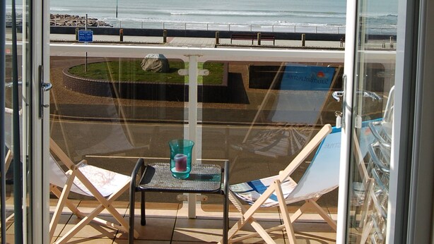 Ein Balkon mit Meerblick, ein Glastisch mit Stuhl und ein blaues Schild.