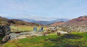 Un patio con paredes de piedra, mobiliario exterior y vistas a colinas ondulantes.