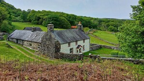 A stone house with a sloped roof, surrounded by lush green fields and trees. - Gallestra a Rustic, Rural Retreat Farm House Nr Dolgellau Snowdonia (Dolgellau)