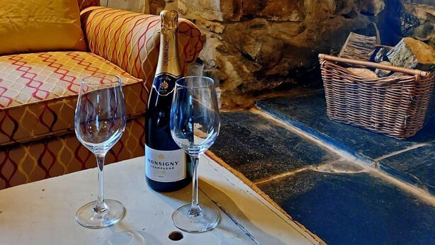 A stone wall, a wooden door, a sofa with patterned cushions, a table with a bottle of champagne and two glasses, a lamp, and a wicker basket. - Gallestra a Rustic, Rural Retreat Farm House Nr Dolgellau Snowdonia (Dolgellau)