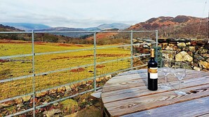 A table with a bottle of wine and two glasses, overlooking a scenic landscape with mountains and a fenced field. - Gallestra a Rustic, Rural Retreat Farm House Nr Dolgellau Snowdonia (Dolgellau)