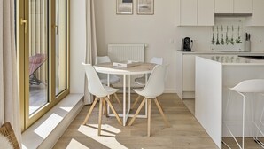 Eine moderne Küche mit weißen Schränken, ein Essbereich mit einem Holztisch und weißen Stühlen sowie ein Blick durch große Schiebeglastüren.