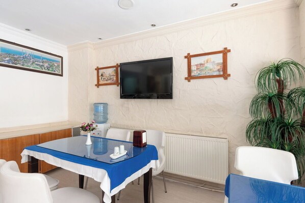 Ett hotellrum med ett matbord, stolar, en tv som är monterad på väggen och en stor krukväxt.