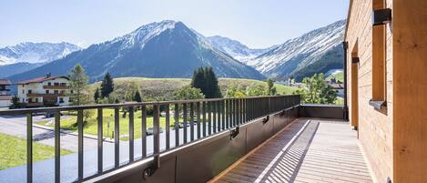 Un balcón con vistas a montañas nevadas, una terraza de madera y una baranda de metal.