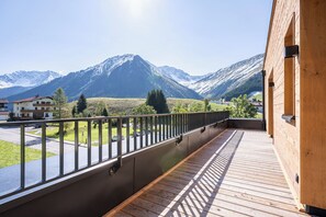 Un balcon offrant une vue sur des montagnes enneigées, une terrasse en bois et une rambarde en métal.