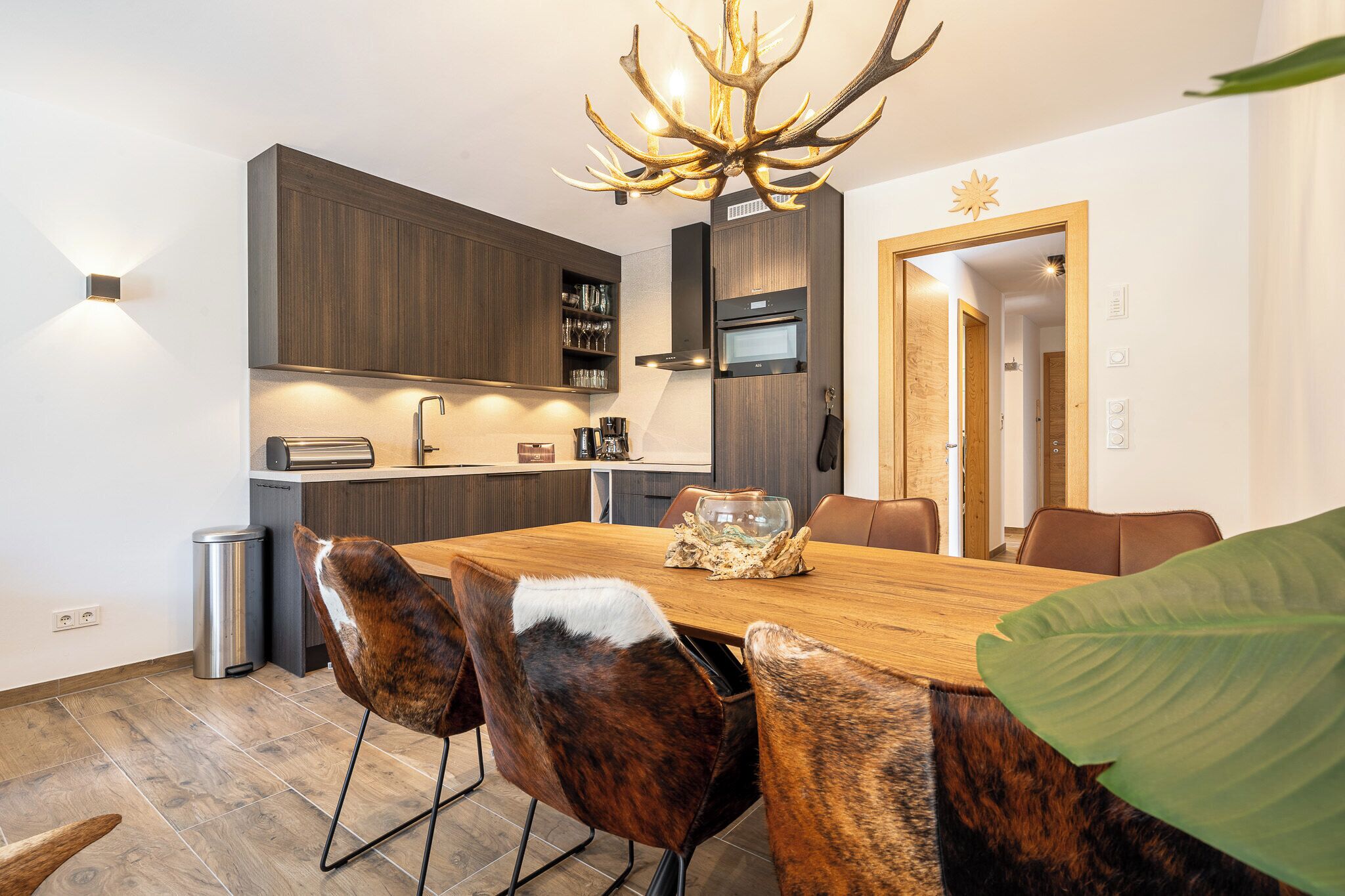 Une cuisine moderne avec des meubles de couleur sombre en bois, un four encastré et un lustre original en forme de bois de cerf.