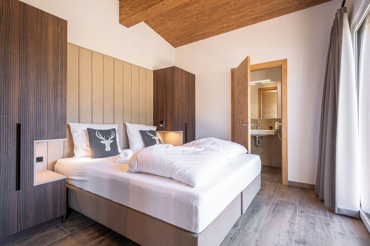 A modern bedroom with a wooden ceiling, a large bed with white bedding, and a built-in wardrobe.