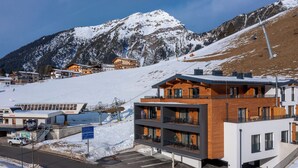Ett modernt hotell med en skidlift i bakgrunden, en parkeringsplats och ett bergigt landskap.