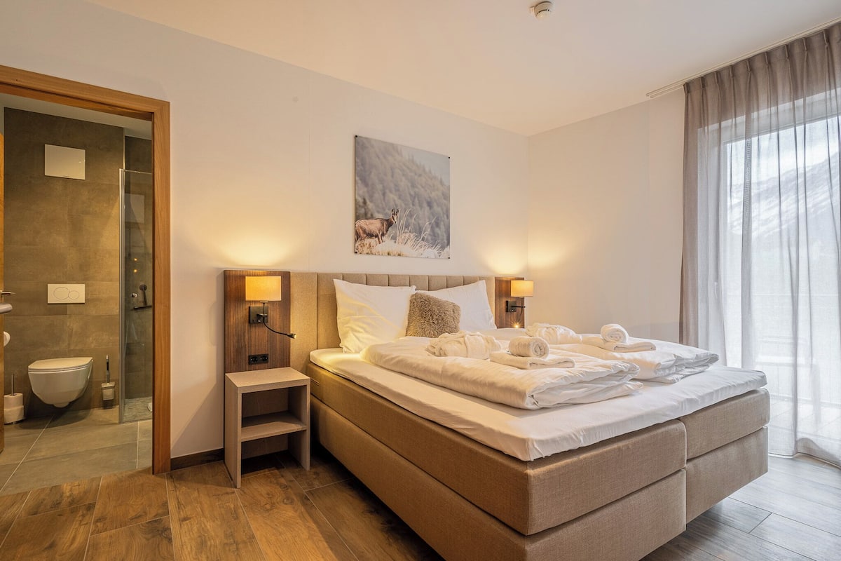 A modern hotel room with a large bed, a glass shower enclosure, and a painting of a deer on the wall.