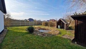 Un jardin avec un petit étang, un abri en bois et une maison dotée d’un toit en pente.