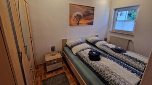 Une chambre à coucher avec un lit, une table de chevet, une armoire, un tableau, une fenêtre et un radiateur.