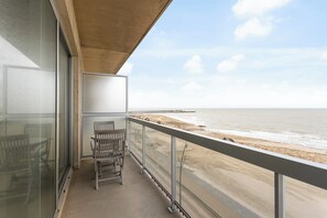 A balcony with a view of the beach, a chair, and a glass door. - Seafront Apartment in Blankenberge (Blankenberge)