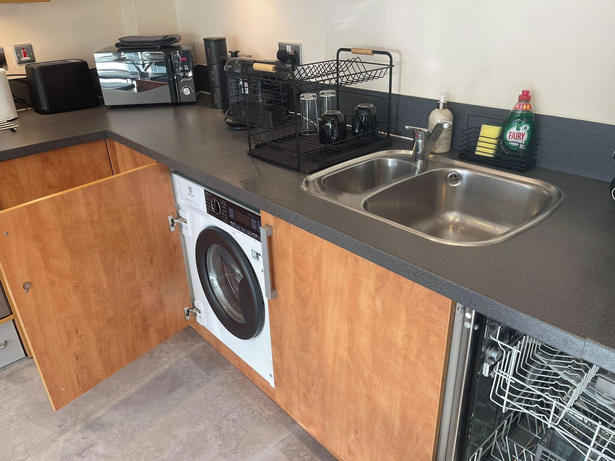 A compact kitchen with a built-in washing machine, a double sink, and a coffee maker.