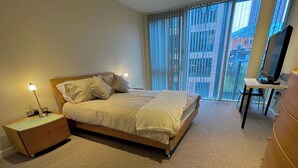 Een hotelkamer met een bed, nachtkastje, lamp en een bureau met stoel.