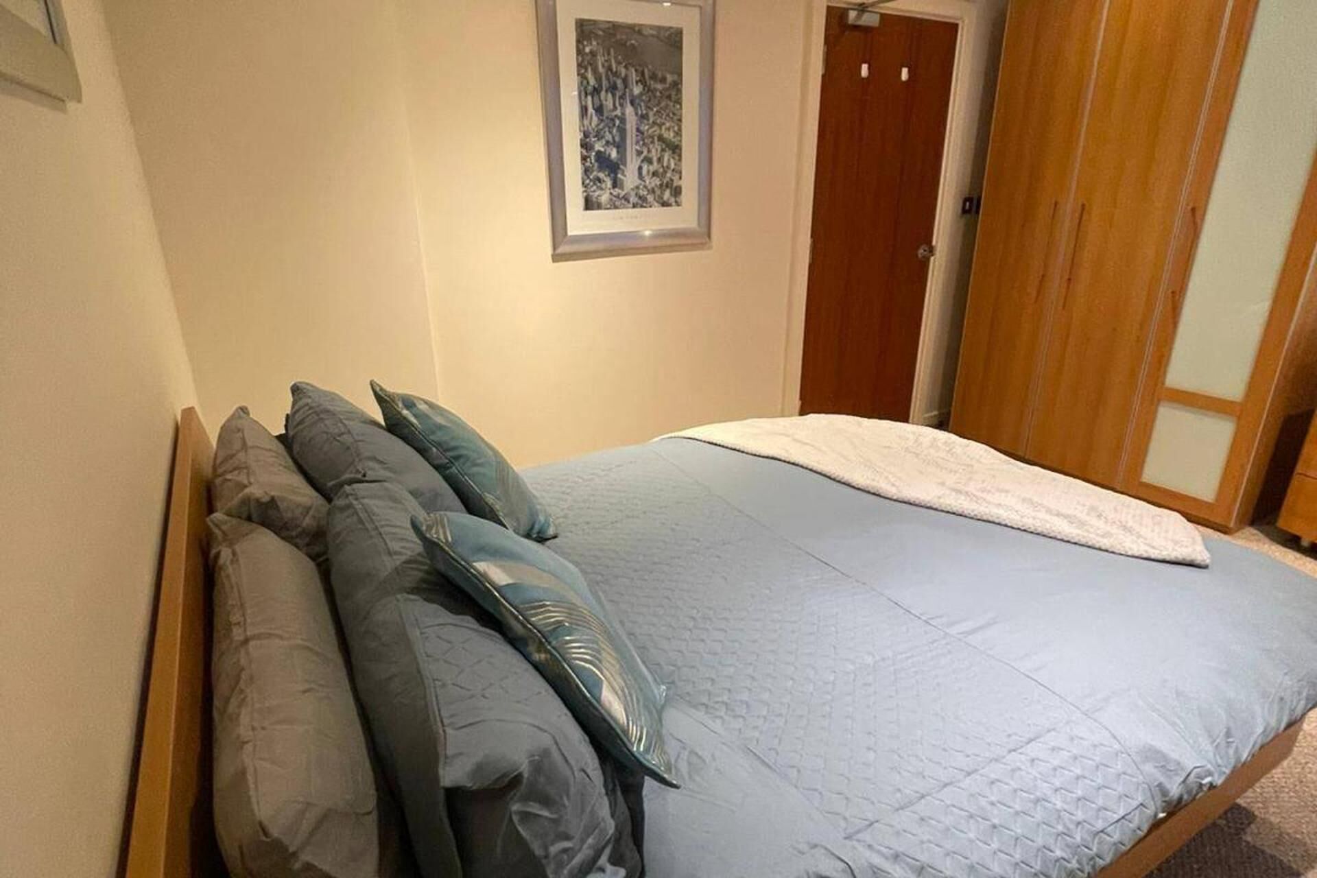 A bedroom with a bed, pillows, a framed picture on the wall, and a wooden door.
