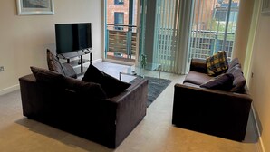 Een moderne woonkamer met twee banken, een flatscreen televisie en een glazen salontafel.