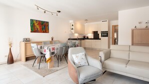 A modern living room with a dining area, a sofa, a coffee table, and a kitchen in the background. - Comfy City Stay Near Sea (Ostend)