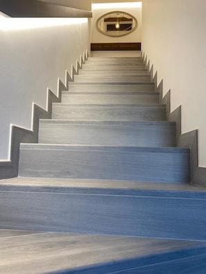 Una escalera de diseño moderno que sube a un rellano con un espejo redondo y una lámpara.