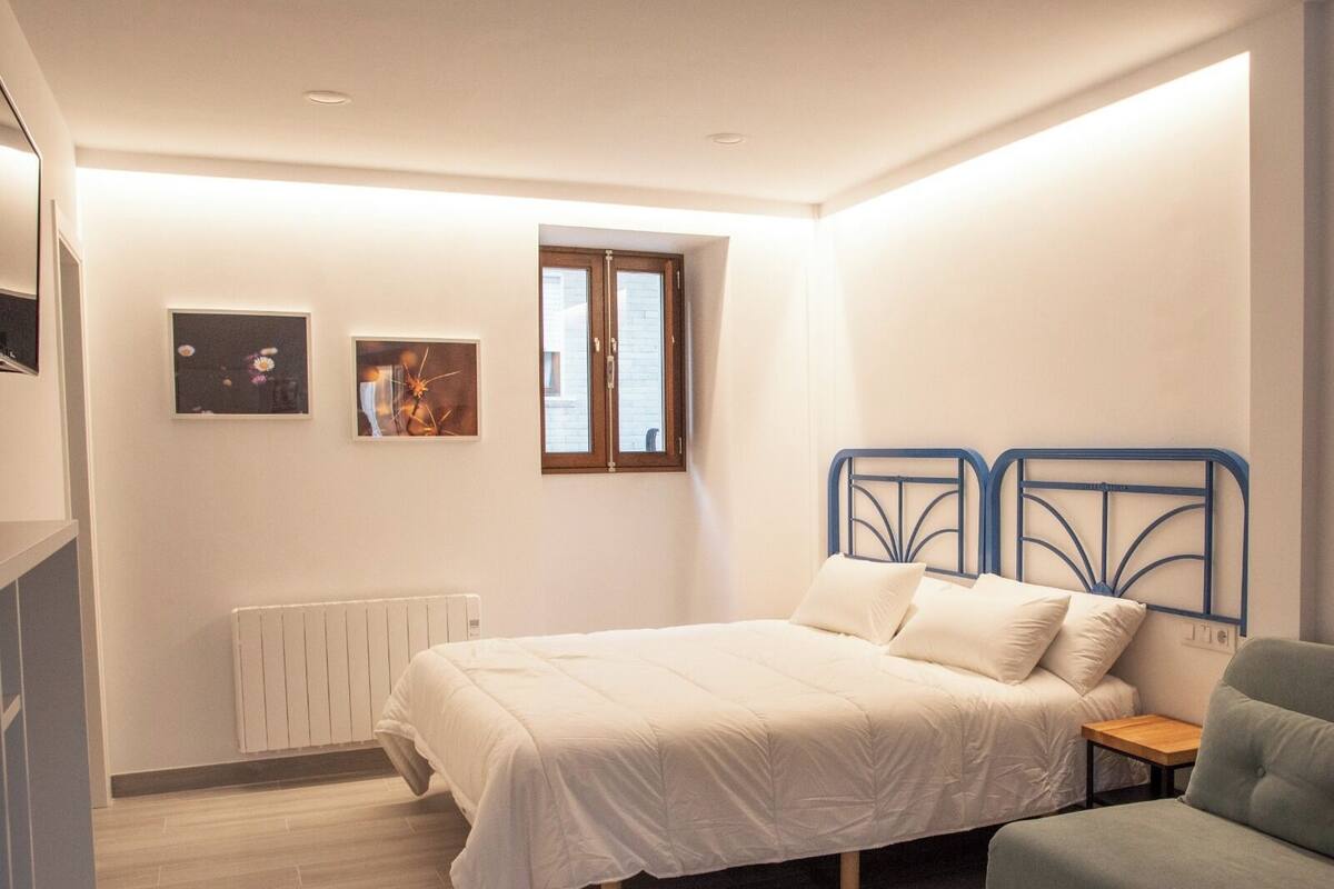 Un dormitorio con cama, una silla, un radiador y dos cuadros colgados en la pared.