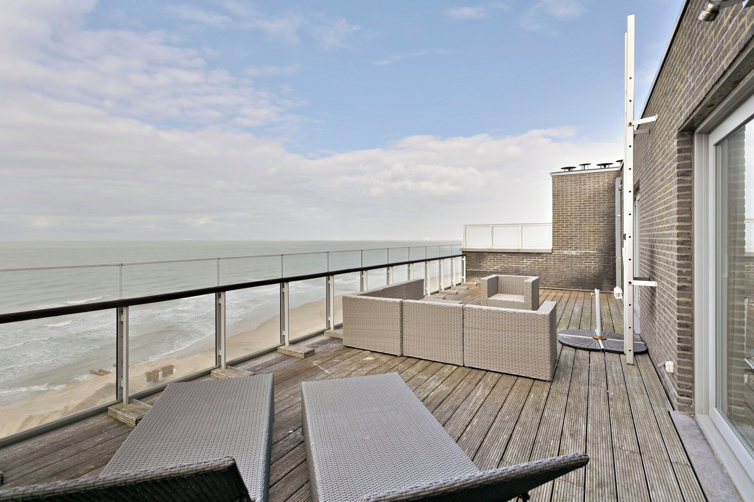 A wooden deck with wicker furniture overlooking the sea.