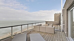 Eine Holzterrasse mit Korbmöbeln und Blick auf das Meer.