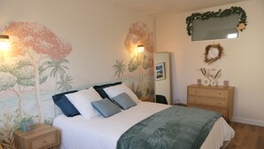 Ein Schlafzimmer mit einem Bett, Nachttischen, einer Kommode, einem Spiegel und Wandbildern.