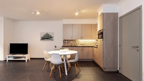 A modern kitchen with a dining area, featuring a round table with chairs, a flat-screen TV, and a tiled backsplash.