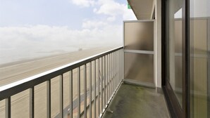 Ein Balkon mit Metallgeländer, einer Glastür und Blick auf Strand und Himmel.
