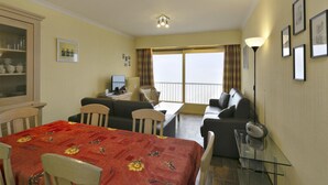 Ein Hotelzimmer mit Essbereich, einer Couch, einem Fernseher und einem Balkon mit Vorhängen.