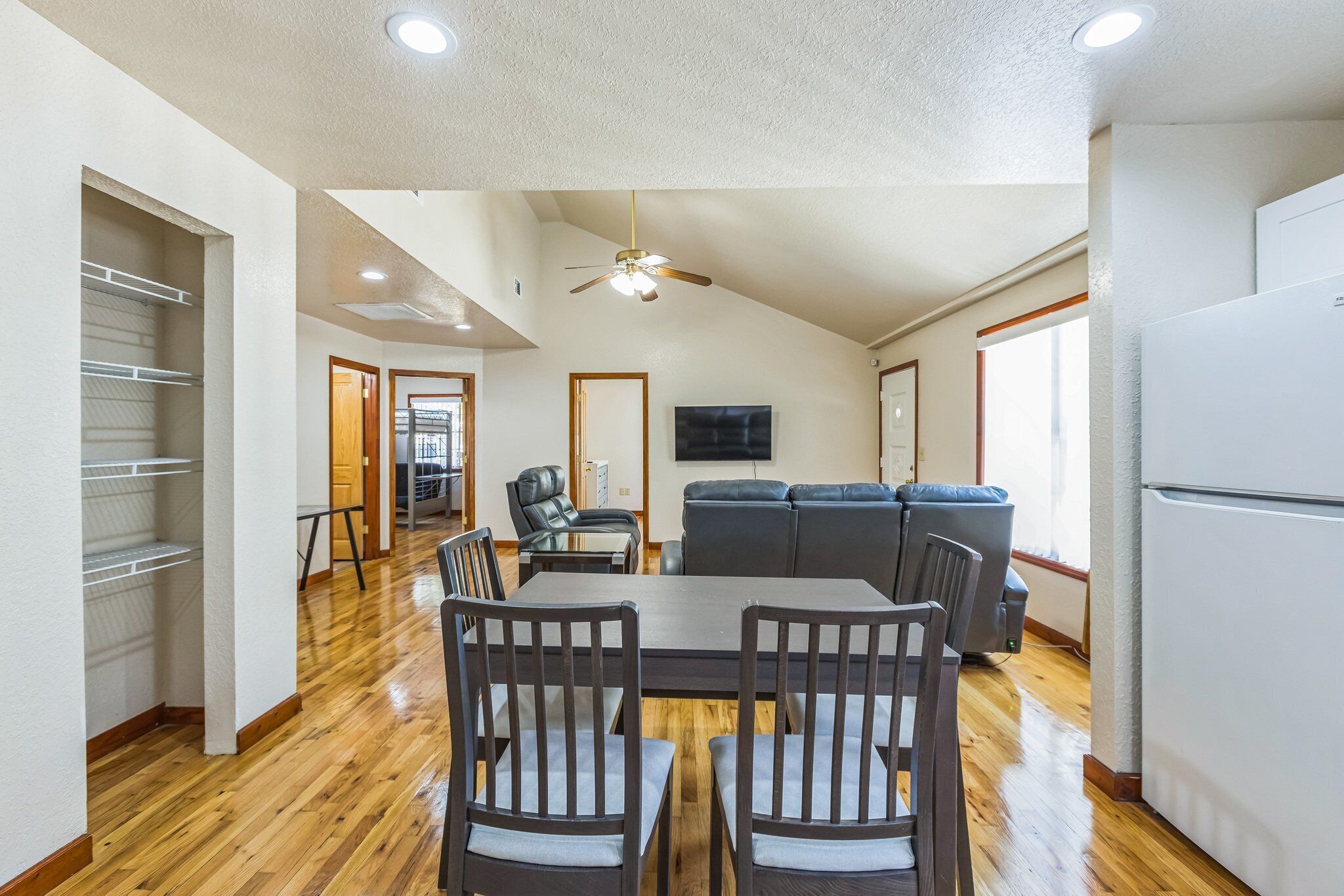 A spacious living area with a dining table, chairs, a sofa, and a ceiling fan.