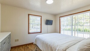 A bedroom with a bed, a TV mounted on the wall, and a window with blinds.