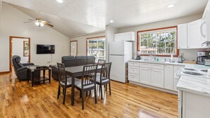 A spacious living room with a wooden floor, a gray sofa, a dining table with chairs, and a ceiling fan.