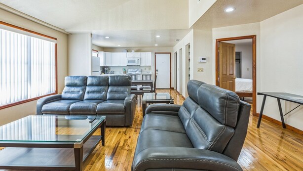 A spacious living room with leather sofas, a glass coffee table, and a ceiling fan.