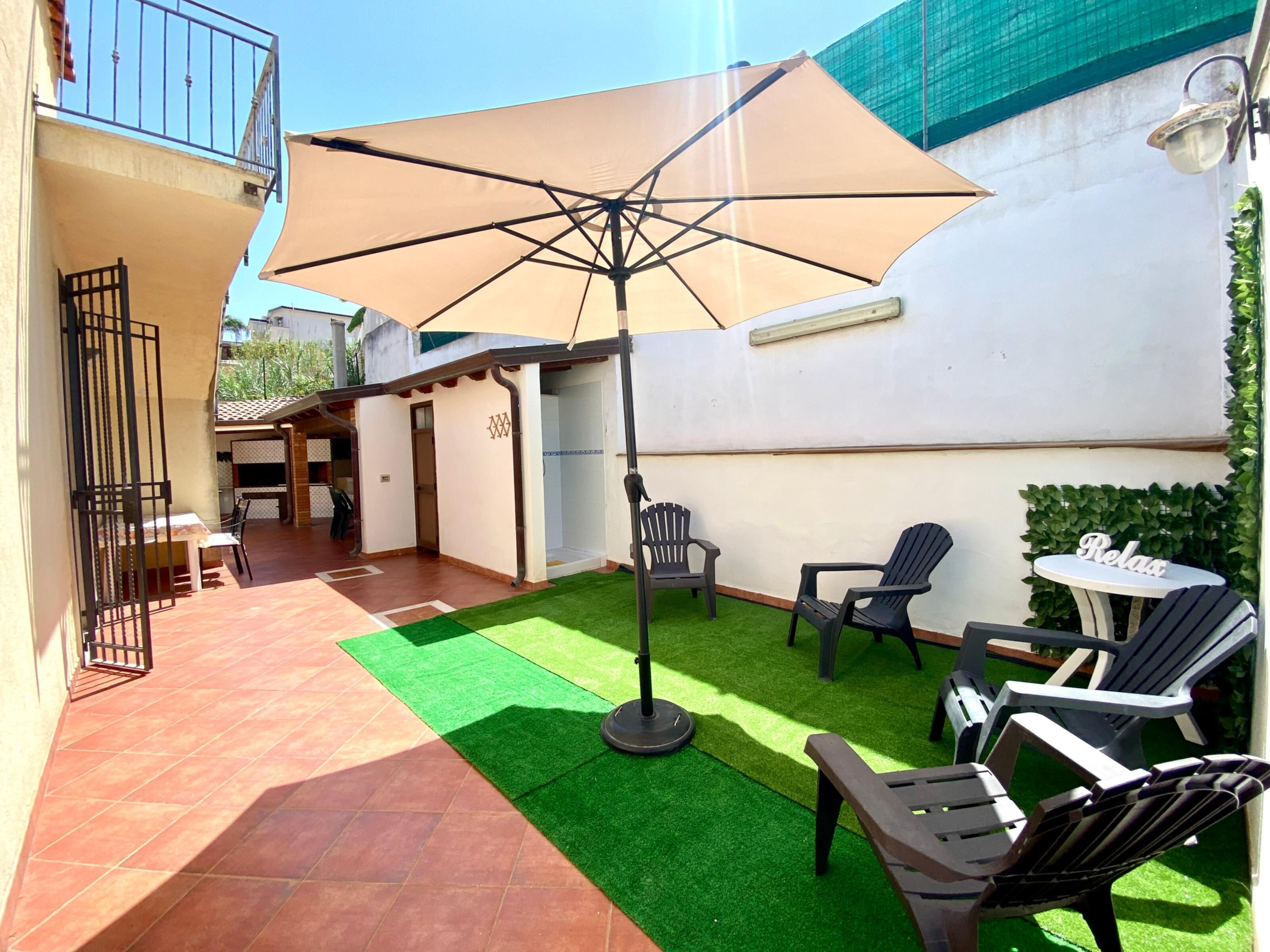 Un patio con una sombrilla grande, mobiliario exterior y césped artificial.