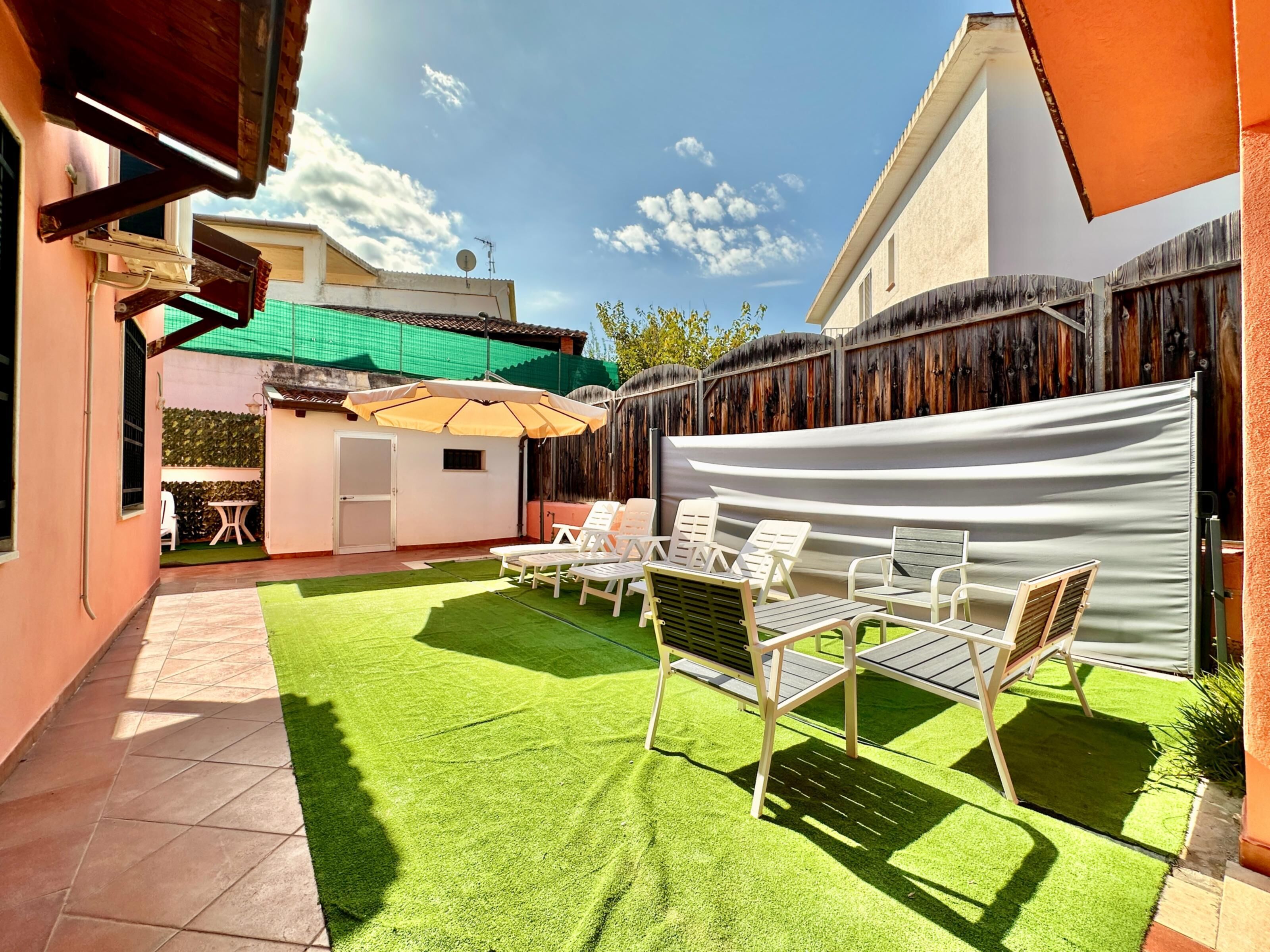 Eine Terrasse mit Kunstgrasanlage, weißen Lounge-Sesseln und einem Tisch.