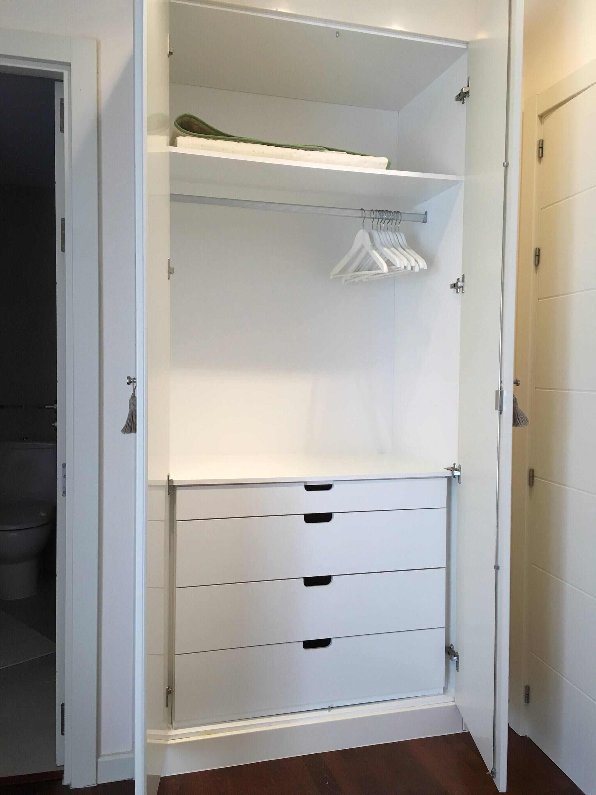 A walk-in closet with open doors, featuring a hanging rod, multiple drawers, and a small shelf.