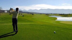 Une personne jouant au golf sur un terrain bien entretenu, avec un étang et des montagnes en arrière-plan.