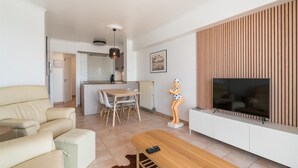 Un salon moderne avec un canapé, une table basse en bois, un téléviseur et un coin cuisine à l’arrière-plan.