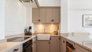 Une cuisine moderne avec des carreaux de métro blancs, des meubles de couleur beige, un four encastré et un évier blanc.