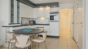 A modern kitchen with white cabinets, a built-in microwave, and a dining area with a round table and four chairs. - Luxbeach Apartment in Blankenberge (Blankenberge)
