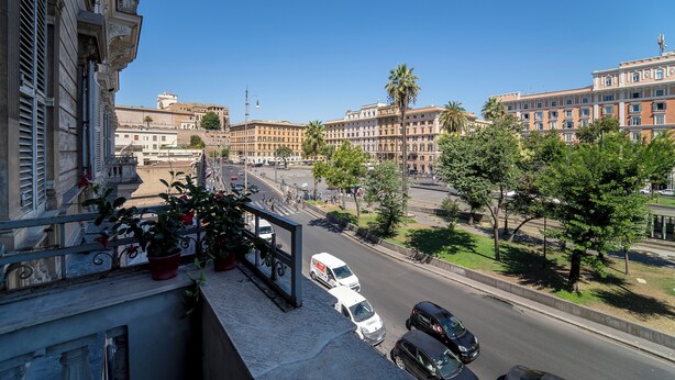 A balcony with potted plants, a view of a busy street with cars, and buildings in the background. - Il Passetto (Rome)