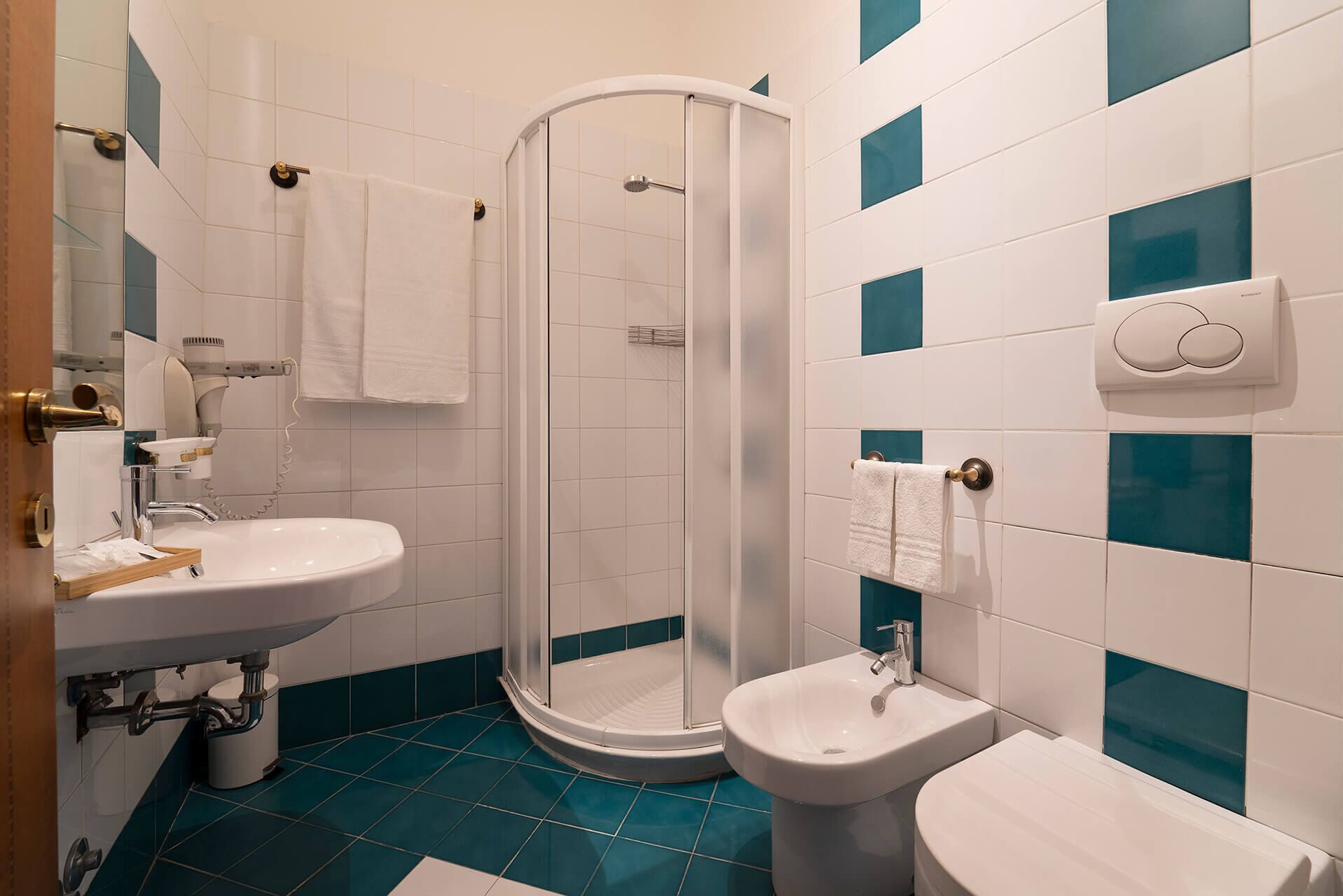 A bathroom with a shower, sink, and toilet, featuring white and teal tiles.