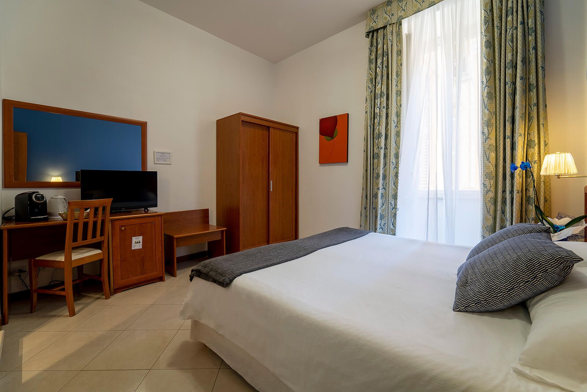 Una habitación de hotel con cama, escritorio con silla, televisor y armario.